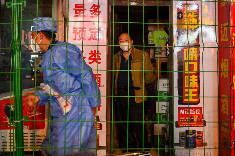 A man looks on from a shop in a neighborhood in lockdown as a worker erects fencing Shanghai's Changning district after new COVID-19 cases were reported, October 7, 2022. Credit: AFP