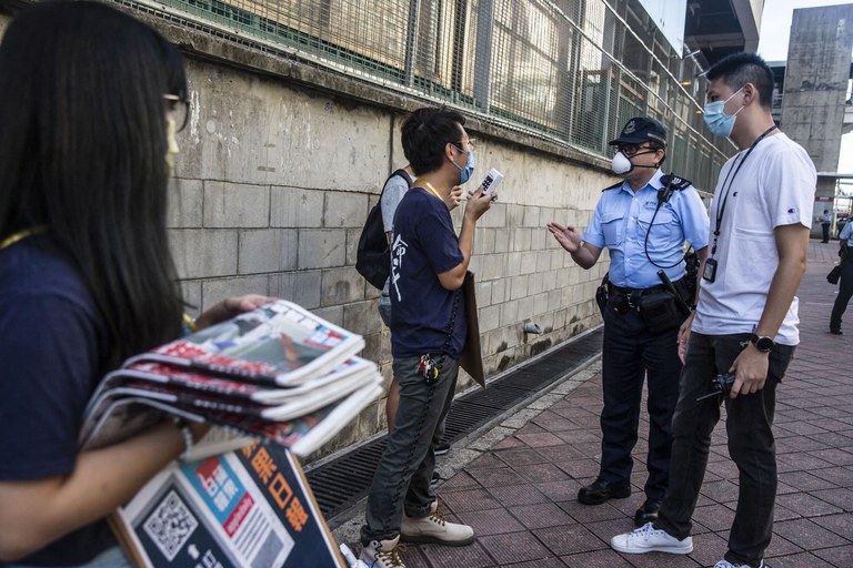 In this Aug. 11, 2020 photo, security officers ask pro-democracy district councilor Ng Kin-wai to not to use a megaphone while volunteers hand out free copies of the Apple Daily newspaper in Hong Kong. Credit: AP