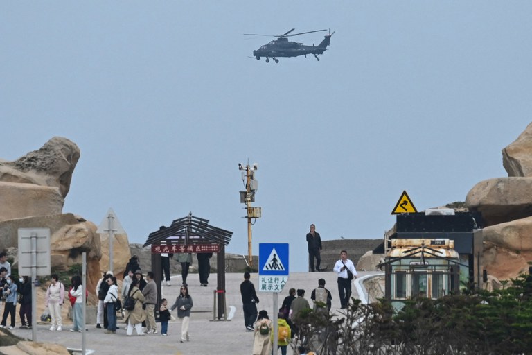 A Chinese military helicopter flies past tourists at a viewing point over the Taiwan Strait, on Pingtan island, the closest point to Taiwan, in China's southeast Fujian province on April 7, 2023. Credit: Greg Baker/AFP