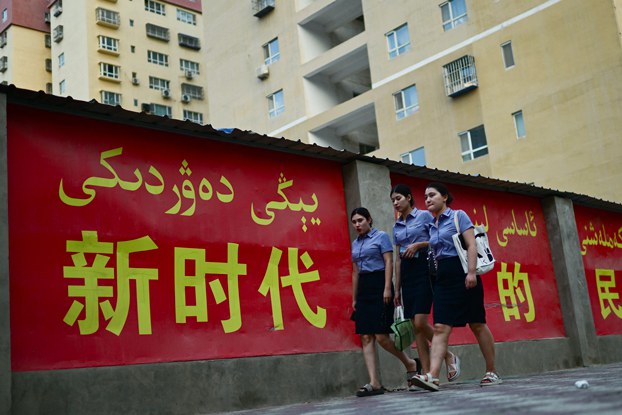 Women walk past a propaganda slogan promoting ethnic unity in 'the new era,' in both Chinese and Uyghur languages, in Yarkand, northwestern China's Xinjiang region, July 18, 2023. Credit: Pedro Paro/AFP