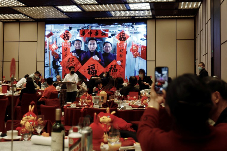 A woman takes pictures of a screen displaying Spring Festival greetings from Chinese astronauts Fei Junlong, Deng Qingming and Zhang Lu aboard China's space station, during a Lunar New Year's Eve dinner service at Shangri-La Shougang Park hotel in Beijing, Jan. 21, 2023. Credit: Florence Lo/Reuters