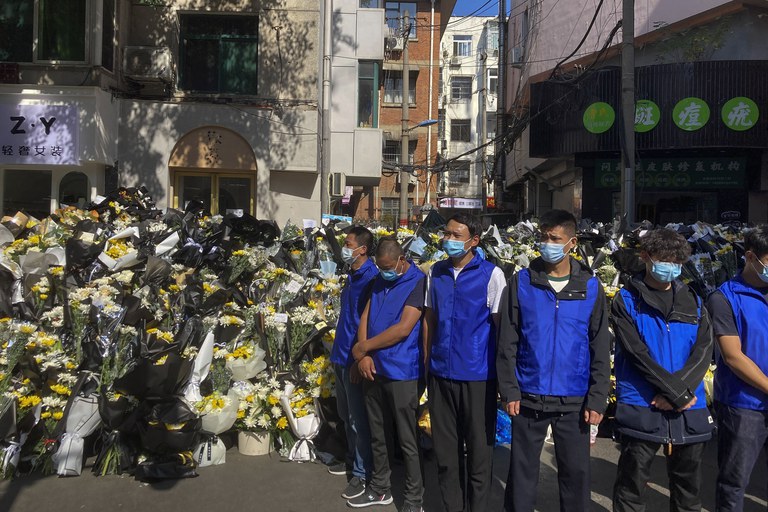 Security personnel in blue vests stand guard in front of the flowers laid by mourners near a residential building where the late Chinese Premier Li Keqiang spent his childhood in Hefei city, in central China's Anhui province, Nov. 2, 2023. Death of once second most-powerful figure in murky circumstances has shocked the Chinese Communist Party throughout its ranks, with a sense of panic and uneasiness plaguing government officials at every level.Credit: Ken Moritsugu/AP