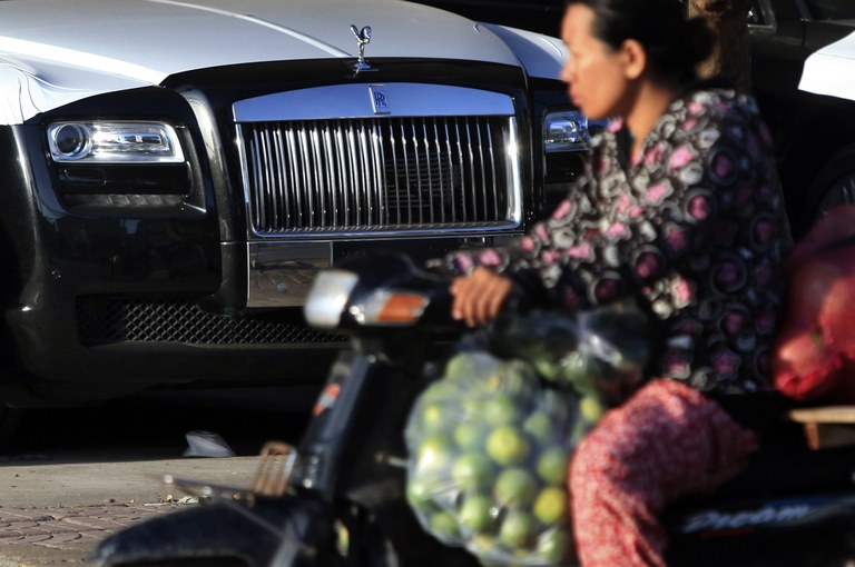 A woman on a motorcycle laden with goods rides past a Rolls-Royce at a car dealership in Phnom Penh in 2014. Credit: Samrang Pring/Reuters